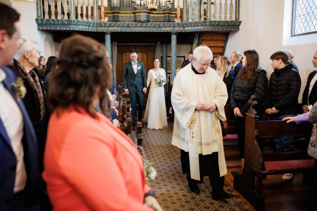Emotionaler Moment bei der kirchlichen Trauung in Wesel: Das Brautpaar steht gemeinsam am Altar, die Braut im weißen Spitzenkleid mit Schleier, der Bräutigam im eleganten Anzug. Gäste verfolgen die Zeremonie in der Kirche aufmerksam. Dieses authentische Hochzeitsfoto hält die besonderen Augenblicke fest und zeigt die lebendige Hochzeitsfotografie in Wesel.