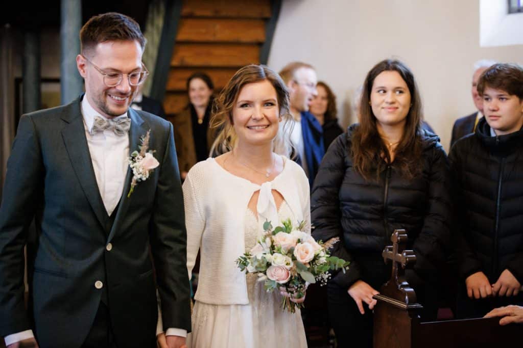 Emotionaler Moment bei der kirchlichen Trauung in Wesel: Das Brautpaar steht gemeinsam am Altar, die Braut im weißen Spitzenkleid mit Schleier, der Bräutigam im eleganten Anzug. Gäste verfolgen die Zeremonie in der Kirche aufmerksam. Dieses authentische Hochzeitsfoto hält die besonderen Augenblicke fest und zeigt die lebendige Hochzeitsfotografie in Wesel.