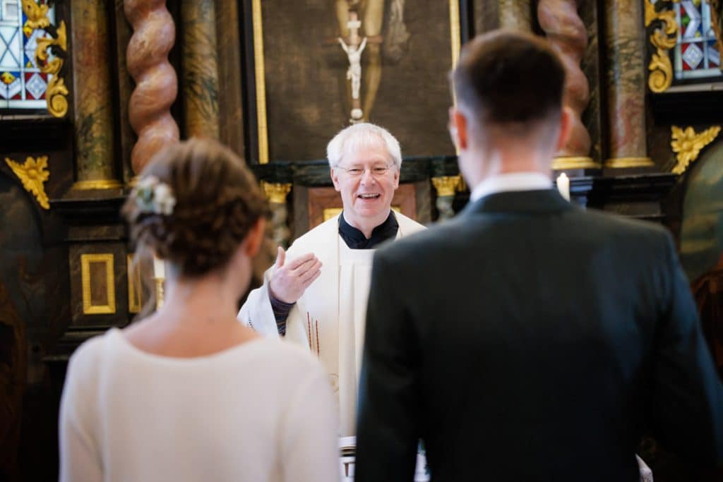 Emotionaler Moment bei der kirchlichen Trauung in Wesel: Das Brautpaar steht gemeinsam am Altar, die Braut im weißen Spitzenkleid mit Schleier, der Bräutigam im eleganten Anzug. Gäste verfolgen die Zeremonie in der Kirche aufmerksam. Dieses authentische Hochzeitsfoto hält die besonderen Augenblicke fest und zeigt die lebendige Hochzeitsfotografie in Wesel.