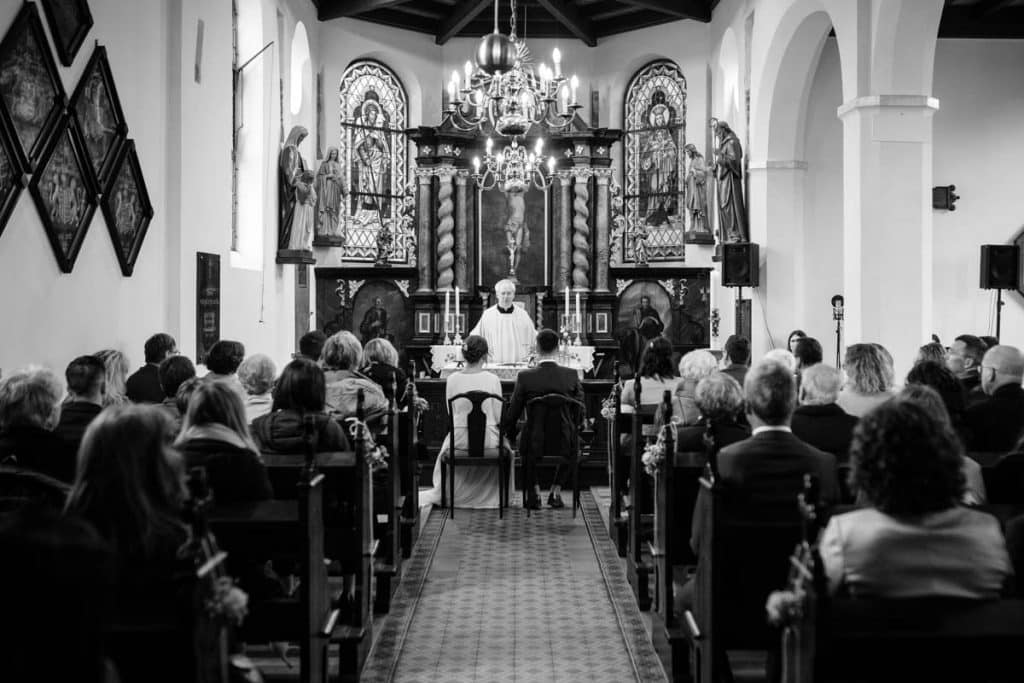 Emotionaler Moment bei der kirchlichen Trauung in Wesel: Das Brautpaar steht gemeinsam am Altar, die Braut im weißen Spitzenkleid mit Schleier, der Bräutigam im eleganten Anzug. Gäste verfolgen die Zeremonie in der Kirche aufmerksam. Dieses authentische Hochzeitsfoto hält die besonderen Augenblicke fest und zeigt die lebendige Hochzeitsfotografie in Wesel.