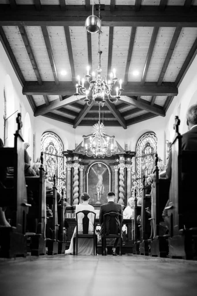 Emotionaler Moment bei der kirchlichen Trauung in Wesel: Das Brautpaar steht gemeinsam am Altar, die Braut im weißen Spitzenkleid mit Schleier, der Bräutigam im eleganten Anzug. Gäste verfolgen die Zeremonie in der Kirche aufmerksam. Dieses authentische Hochzeitsfoto hält die besonderen Augenblicke fest und zeigt die lebendige Hochzeitsfotografie in Wesel.