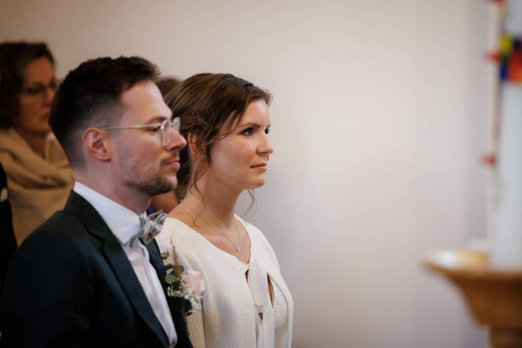 Emotionaler Moment bei der kirchlichen Trauung in Wesel: Das Brautpaar steht gemeinsam am Altar, die Braut im weißen Spitzenkleid mit Schleier, der Bräutigam im eleganten Anzug. Gäste verfolgen die Zeremonie in der Kirche aufmerksam. Dieses authentische Hochzeitsfoto hält die besonderen Augenblicke fest und zeigt die lebendige Hochzeitsfotografie in Wesel.