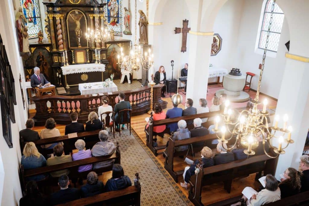 Emotionaler Moment bei der kirchlichen Trauung in Wesel: Das Brautpaar steht gemeinsam am Altar, die Braut im weißen Spitzenkleid mit Schleier, der Bräutigam im eleganten Anzug. Gäste verfolgen die Zeremonie in der Kirche aufmerksam. Dieses authentische Hochzeitsfoto hält die besonderen Augenblicke fest und zeigt die lebendige Hochzeitsfotografie in Wesel.