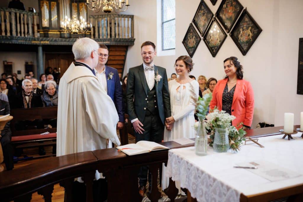 Emotionaler Moment bei der kirchlichen Trauung in Wesel: Das Brautpaar steht gemeinsam am Altar, die Braut im weißen Spitzenkleid mit Schleier, der Bräutigam im eleganten Anzug. Gäste verfolgen die Zeremonie in der Kirche aufmerksam. Dieses authentische Hochzeitsfoto hält die besonderen Augenblicke fest und zeigt die lebendige Hochzeitsfotografie in Wesel.
