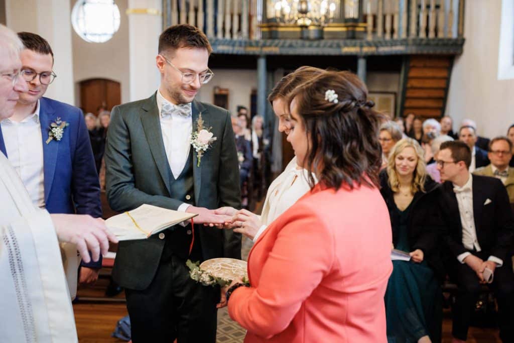 Emotionaler Moment bei der kirchlichen Trauung in Wesel: Das Brautpaar steht gemeinsam am Altar, die Braut im weißen Spitzenkleid mit Schleier, der Bräutigam im eleganten Anzug. Gäste verfolgen die Zeremonie in der Kirche aufmerksam. Dieses authentische Hochzeitsfoto hält die besonderen Augenblicke fest und zeigt die lebendige Hochzeitsfotografie in Wesel.