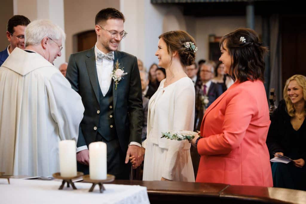 Emotionaler Moment bei der kirchlichen Trauung in Wesel: Das Brautpaar steht gemeinsam am Altar, die Braut im weißen Spitzenkleid mit Schleier, der Bräutigam im eleganten Anzug. Gäste verfolgen die Zeremonie in der Kirche aufmerksam. Dieses authentische Hochzeitsfoto hält die besonderen Augenblicke fest und zeigt die lebendige Hochzeitsfotografie in Wesel.