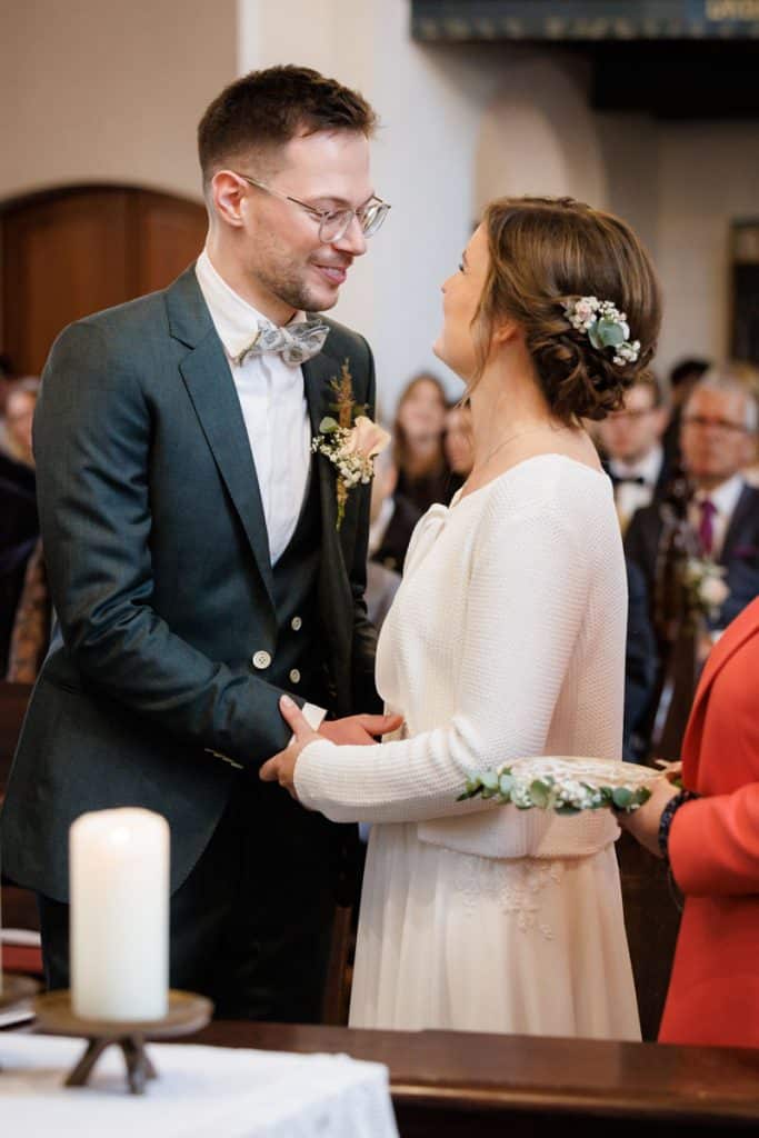 Emotionaler Moment bei der kirchlichen Trauung in Wesel: Das Brautpaar steht gemeinsam am Altar, die Braut im weißen Spitzenkleid mit Schleier, der Bräutigam im eleganten Anzug. Gäste verfolgen die Zeremonie in der Kirche aufmerksam. Dieses authentische Hochzeitsfoto hält die besonderen Augenblicke fest und zeigt die lebendige Hochzeitsfotografie in Wesel.