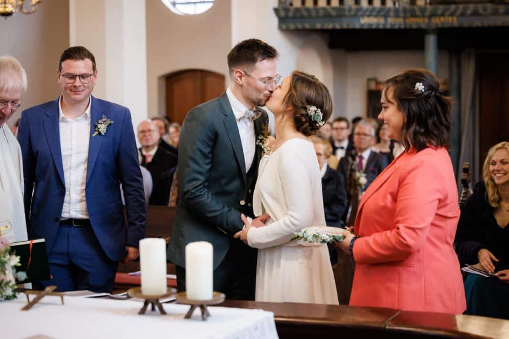 Emotionaler Moment bei der kirchlichen Trauung in Wesel: Das Brautpaar steht gemeinsam am Altar, die Braut im weißen Spitzenkleid mit Schleier, der Bräutigam im eleganten Anzug. Gäste verfolgen die Zeremonie in der Kirche aufmerksam. Dieses authentische Hochzeitsfoto hält die besonderen Augenblicke fest und zeigt die lebendige Hochzeitsfotografie in Wesel.