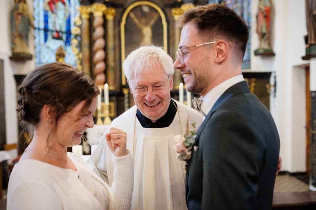 Emotionaler Moment bei der kirchlichen Trauung in Wesel: Das Brautpaar steht gemeinsam am Altar, die Braut im weißen Spitzenkleid mit Schleier, der Bräutigam im eleganten Anzug. Gäste verfolgen die Zeremonie in der Kirche aufmerksam. Dieses authentische Hochzeitsfoto hält die besonderen Augenblicke fest und zeigt die lebendige Hochzeitsfotografie in Wesel.