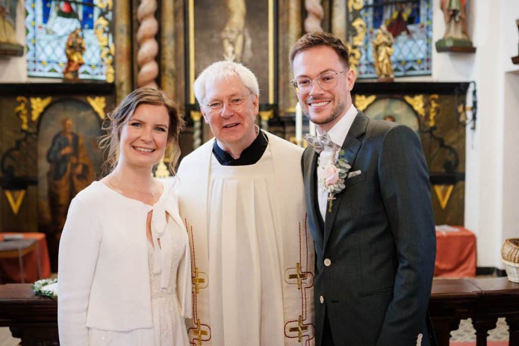 Emotionaler Moment bei der kirchlichen Trauung in Wesel: Das Brautpaar steht gemeinsam am Altar, die Braut im weißen Spitzenkleid mit Schleier, der Bräutigam im eleganten Anzug. Gäste verfolgen die Zeremonie in der Kirche aufmerksam. Dieses authentische Hochzeitsfoto hält die besonderen Augenblicke fest und zeigt die lebendige Hochzeitsfotografie in Wesel.