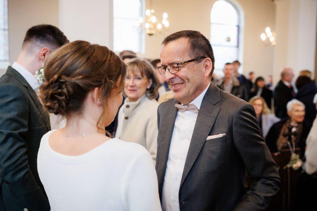 Emotionaler Moment bei der kirchlichen Trauung in Wesel: Das Brautpaar steht gemeinsam am Altar, die Braut im weißen Spitzenkleid mit Schleier, der Bräutigam im eleganten Anzug. Gäste verfolgen die Zeremonie in der Kirche aufmerksam. Dieses authentische Hochzeitsfoto hält die besonderen Augenblicke fest und zeigt die lebendige Hochzeitsfotografie in Wesel.