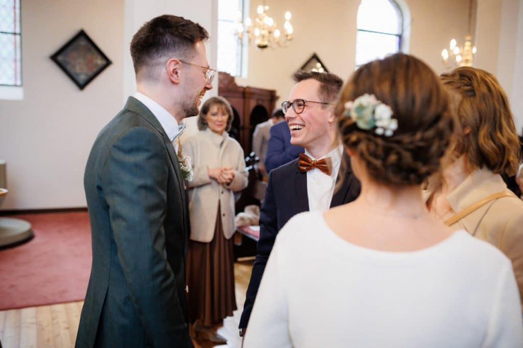 Emotionaler Moment bei der kirchlichen Trauung in Wesel: Das Brautpaar steht gemeinsam am Altar, die Braut im weißen Spitzenkleid mit Schleier, der Bräutigam im eleganten Anzug. Gäste verfolgen die Zeremonie in der Kirche aufmerksam. Dieses authentische Hochzeitsfoto hält die besonderen Augenblicke fest und zeigt die lebendige Hochzeitsfotografie in Wesel.