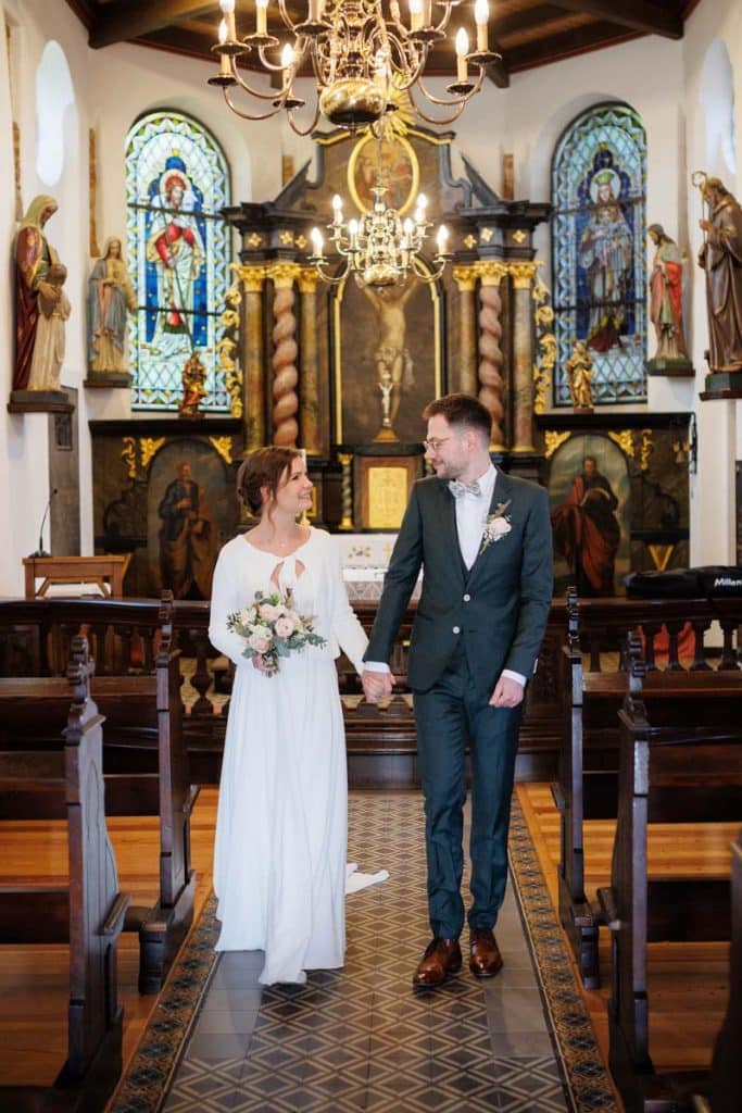 Emotionaler Moment bei der kirchlichen Trauung in Wesel: Das Brautpaar steht gemeinsam am Altar, die Braut im weißen Spitzenkleid mit Schleier, der Bräutigam im eleganten Anzug. Gäste verfolgen die Zeremonie in der Kirche aufmerksam. Dieses authentische Hochzeitsfoto hält die besonderen Augenblicke fest und zeigt die lebendige Hochzeitsfotografie in Wesel.