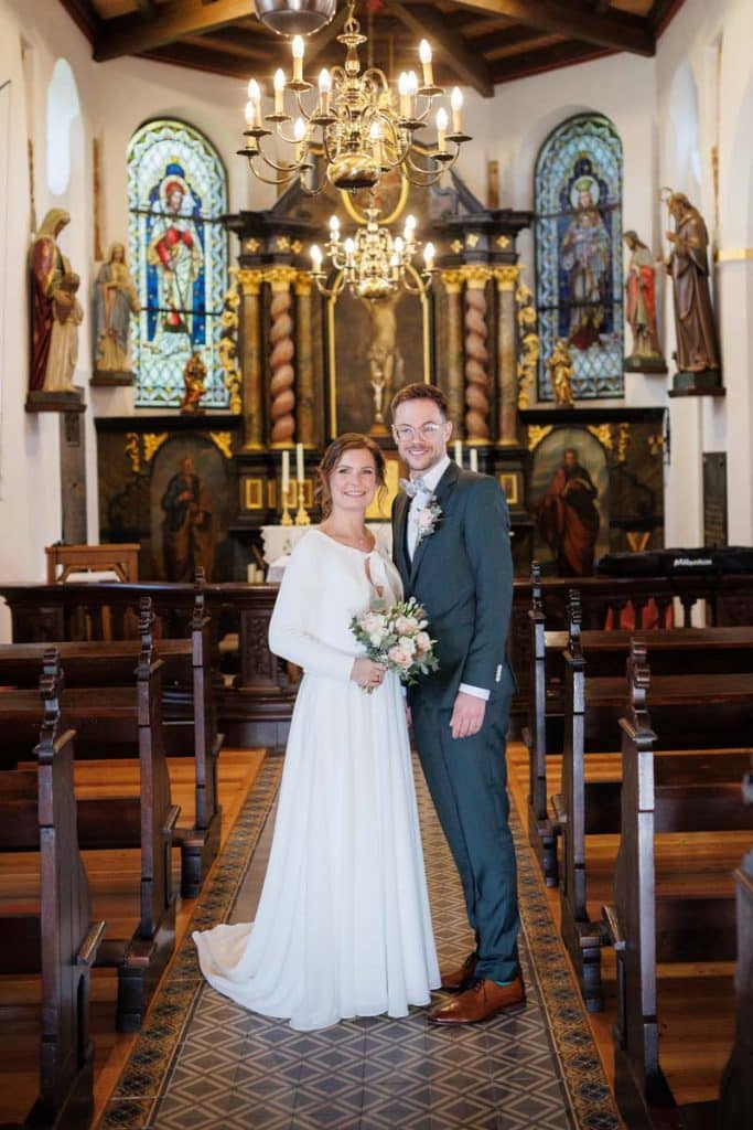 Emotionaler Moment bei der kirchlichen Trauung in Wesel: Das Brautpaar steht gemeinsam am Altar, die Braut im weißen Spitzenkleid mit Schleier, der Bräutigam im eleganten Anzug. Gäste verfolgen die Zeremonie in der Kirche aufmerksam. Dieses authentische Hochzeitsfoto hält die besonderen Augenblicke fest und zeigt die lebendige Hochzeitsfotografie in Wesel.