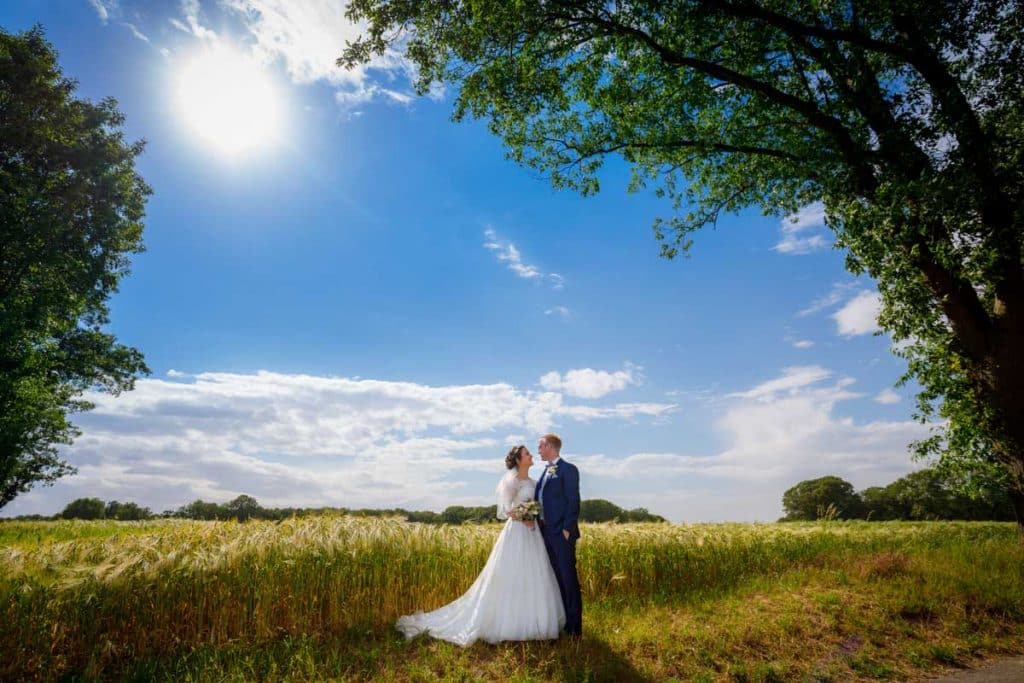 Romantisches Brautpaarshooting im Kurpark in Xanten: Die Braut im eleganten Spitzenkleid und der Bräutigam im festlichen Anzug spazieren Hand in Hand durch die Parkanlage. Sonnenlicht, grüne Bäume und Blumenrabatten schaffen eine idyllische Kulisse. Dieses Foto zeigt die natürliche und moderne Hochzeitsfotografie vom Hochzeitsfotograf Xanten.