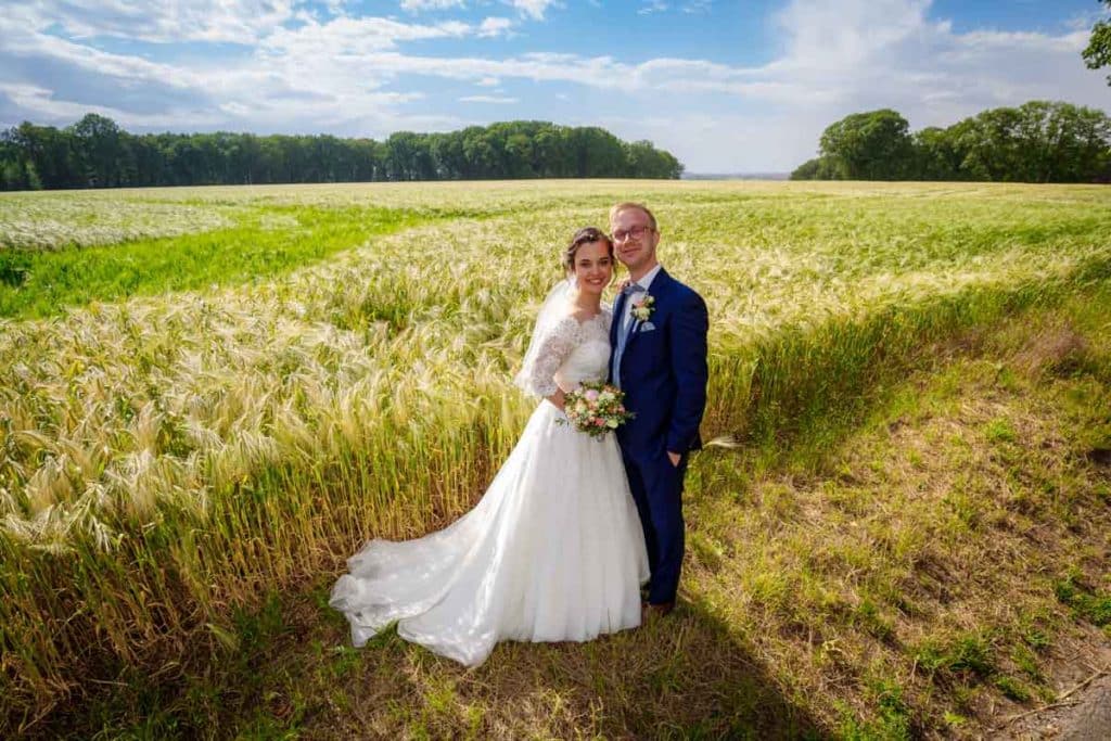 Romantisches Brautpaarshooting im Kurpark in Xanten: Die Braut im eleganten Spitzenkleid und der Bräutigam im festlichen Anzug spazieren Hand in Hand durch die Parkanlage. Sonnenlicht, grüne Bäume und Blumenrabatten schaffen eine idyllische Kulisse. Dieses Foto zeigt die natürliche und moderne Hochzeitsfotografie vom Hochzeitsfotograf Xanten.