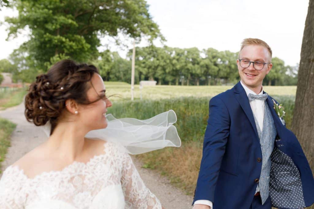 Romantisches Brautpaarshooting im Kurpark in Xanten: Die Braut im eleganten Spitzenkleid und der Bräutigam im festlichen Anzug spazieren Hand in Hand durch die Parkanlage. Sonnenlicht, grüne Bäume und Blumenrabatten schaffen eine idyllische Kulisse. Dieses Foto zeigt die natürliche und moderne Hochzeitsfotografie vom Hochzeitsfotograf Xanten.