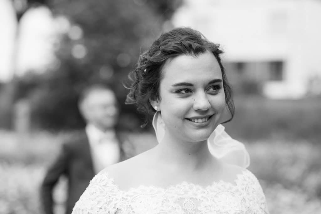 Romantisches Brautpaarshooting im Kurpark in Xanten: Die Braut im eleganten Spitzenkleid und der Bräutigam im festlichen Anzug spazieren Hand in Hand durch die Parkanlage. Sonnenlicht, grüne Bäume und Blumenrabatten schaffen eine idyllische Kulisse. Dieses Foto zeigt die natürliche und moderne Hochzeitsfotografie vom Hochzeitsfotograf Xanten.
