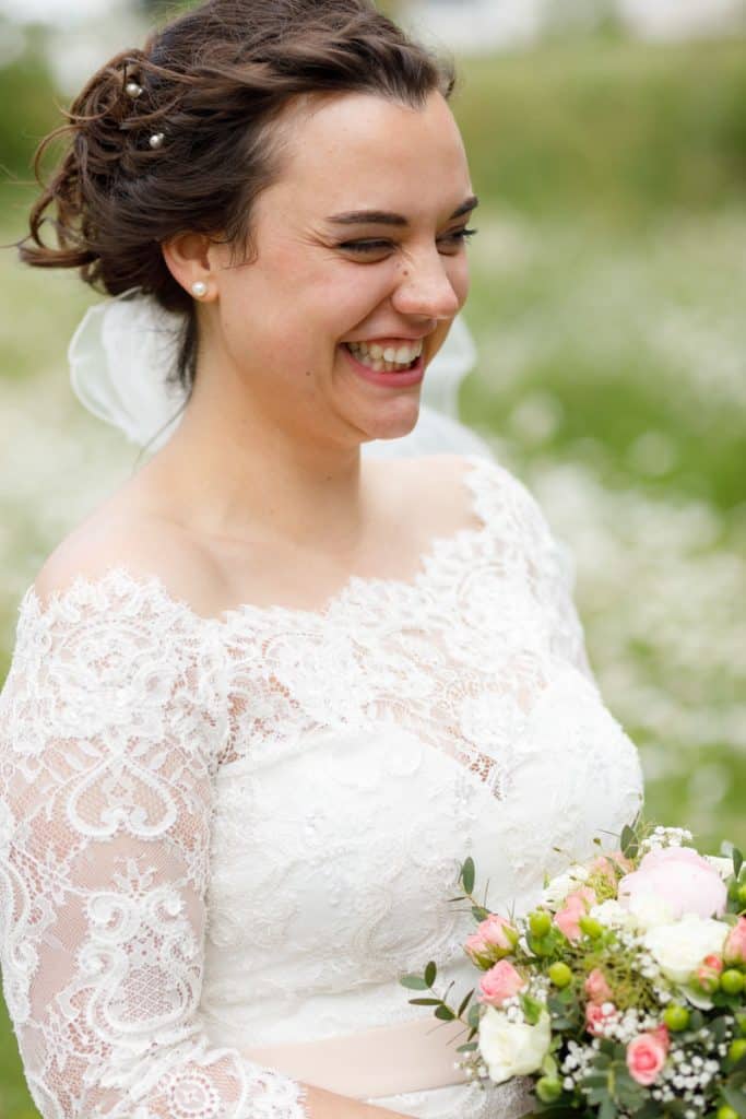 Romantisches Brautpaarshooting im Kurpark in Xanten: Die Braut im eleganten Spitzenkleid und der Bräutigam im festlichen Anzug spazieren Hand in Hand durch die Parkanlage. Sonnenlicht, grüne Bäume und Blumenrabatten schaffen eine idyllische Kulisse. Dieses Foto zeigt die natürliche und moderne Hochzeitsfotografie vom Hochzeitsfotograf Xanten.
