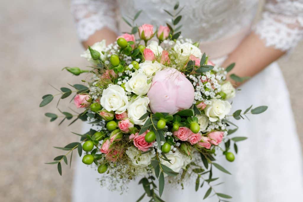 Romantisches Brautpaarshooting im Kurpark in Xanten: Die Braut im eleganten Spitzenkleid und der Bräutigam im festlichen Anzug spazieren Hand in Hand durch die Parkanlage. Sonnenlicht, grüne Bäume und Blumenrabatten schaffen eine idyllische Kulisse. Dieses Foto zeigt die natürliche und moderne Hochzeitsfotografie vom Hochzeitsfotograf Xanten.