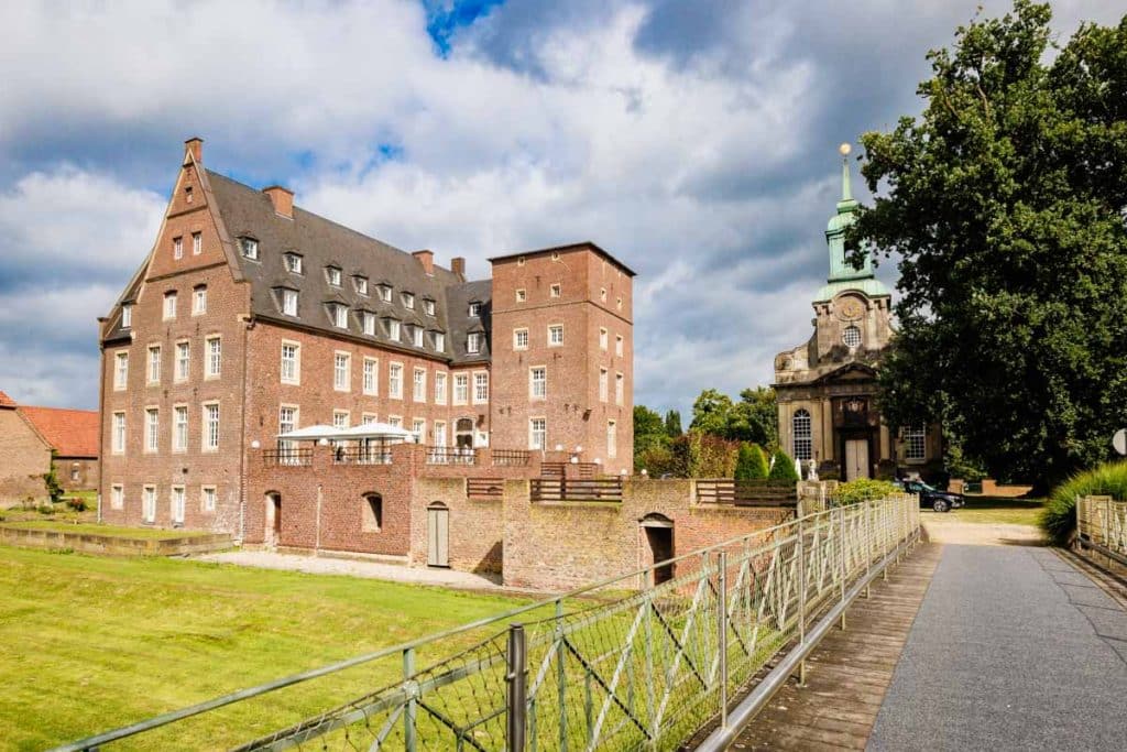 Emotionaler First Look von Braut und Bräutigam auf Schloss Diersfordt in Wesel: Der Bräutigam sieht seine Braut zum ersten Mal im weißen Kleid. Die historische Schlosskulisse sorgt für eine romantische Atmosphäre. Festgehalten vom Hochzeitsfotograf Wesel.