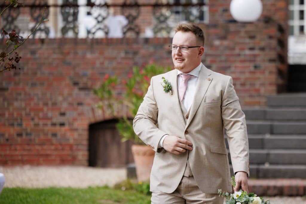 Emotionaler First Look von Braut und Bräutigam auf Schloss Diersfordt in Wesel: Der Bräutigam sieht seine Braut zum ersten Mal im weißen Kleid. Die historische Schlosskulisse sorgt für eine romantische Atmosphäre. Festgehalten vom Hochzeitsfotograf Wesel.