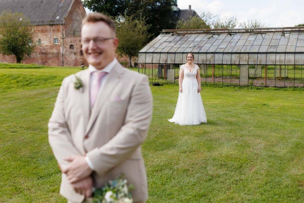 Emotionaler First Look von Braut und Bräutigam auf Schloss Diersfordt in Wesel: Der Bräutigam sieht seine Braut zum ersten Mal im weißen Kleid. Die historische Schlosskulisse sorgt für eine romantische Atmosphäre. Festgehalten vom Hochzeitsfotograf Wesel.