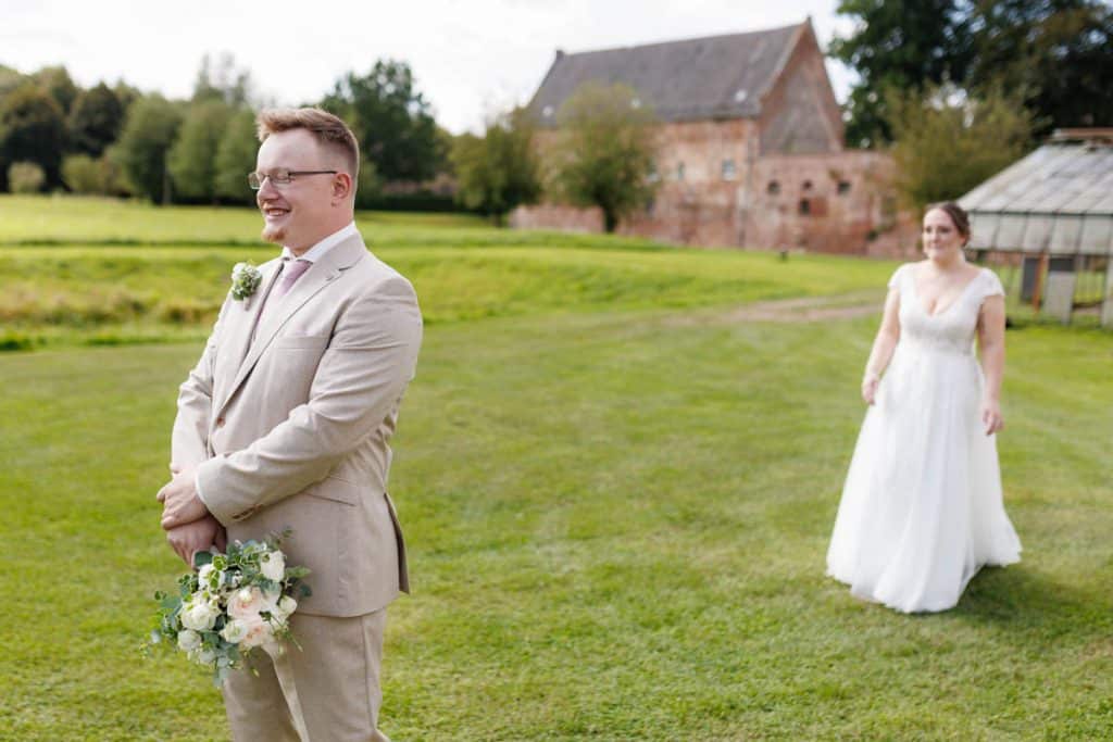 Emotionaler First Look von Braut und Bräutigam auf Schloss Diersfordt in Wesel: Der Bräutigam sieht seine Braut zum ersten Mal im weißen Kleid. Die historische Schlosskulisse sorgt für eine romantische Atmosphäre. Festgehalten vom Hochzeitsfotograf Wesel.