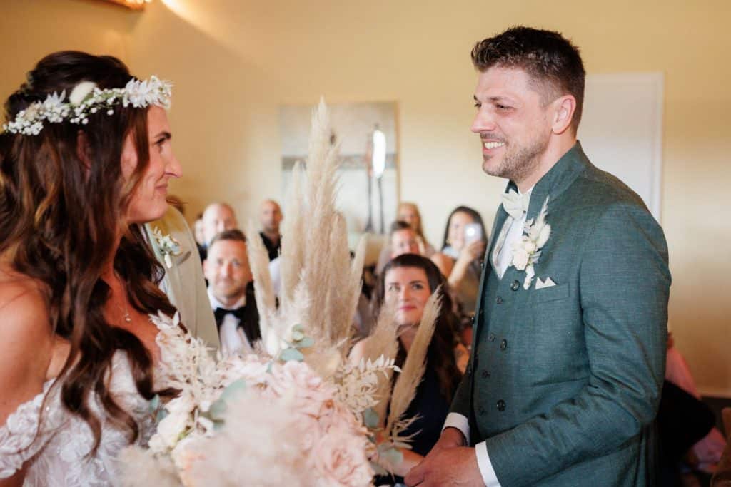 Emotionale freie Trauung im Innenbereich des Landgut Hochwald in Sonsbeck: Das Brautpaar gibt sich vor Familie und Freunden das Ja-Wort. Kerzen, Blumenarrangements und stimmungsvolles Licht sorgen für eine romantische Atmosphäre. Besondere Augenblicke festgehalten vom Hochzeitsfotograf Niederrhein.