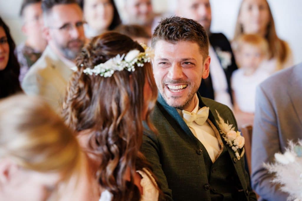 Emotionale freie Trauung im Innenbereich des Landgut Hochwald in Sonsbeck: Das Brautpaar gibt sich vor Familie und Freunden das Ja-Wort. Kerzen, Blumenarrangements und stimmungsvolles Licht sorgen für eine romantische Atmosphäre. Besondere Augenblicke festgehalten vom Hochzeitsfotograf Niederrhein.