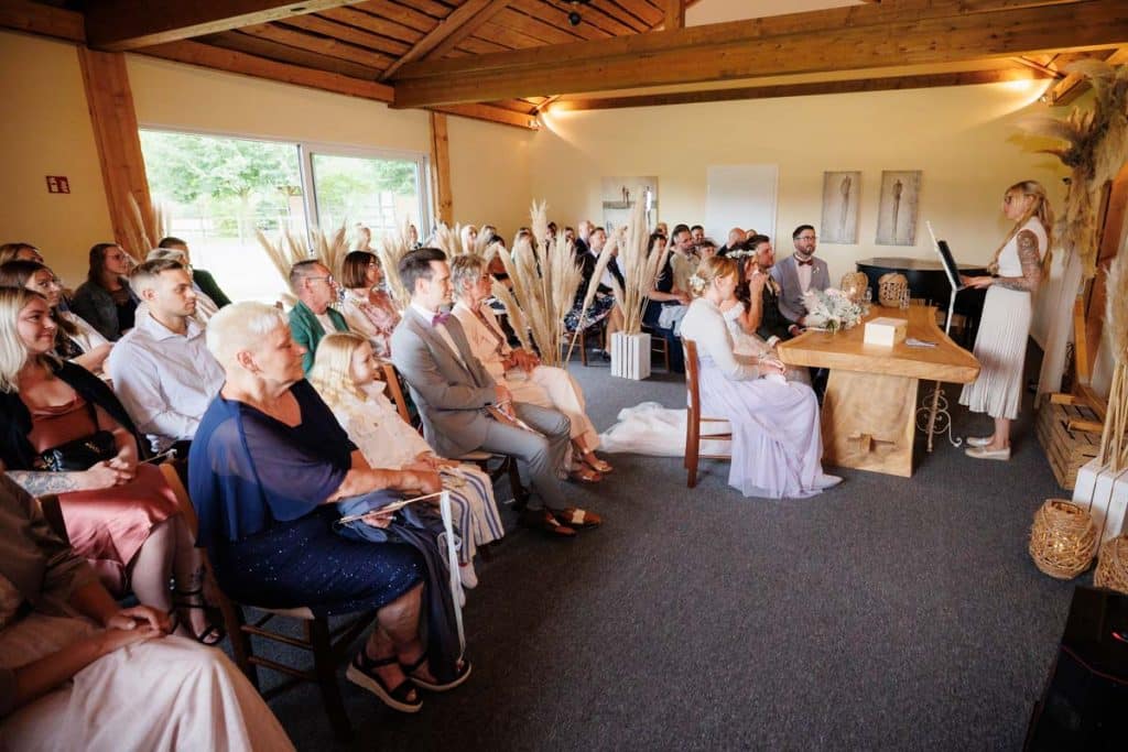 Emotionale freie Trauung im Innenbereich des Landgut Hochwald in Sonsbeck: Das Brautpaar gibt sich vor Familie und Freunden das Ja-Wort. Kerzen, Blumenarrangements und stimmungsvolles Licht sorgen für eine romantische Atmosphäre. Besondere Augenblicke festgehalten vom Hochzeitsfotograf Niederrhein.