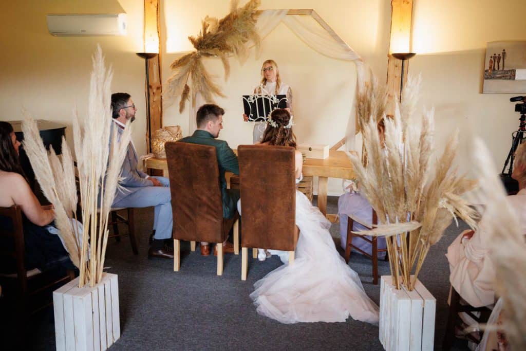 Emotionale freie Trauung im Innenbereich des Landgut Hochwald in Sonsbeck: Das Brautpaar gibt sich vor Familie und Freunden das Ja-Wort. Kerzen, Blumenarrangements und stimmungsvolles Licht sorgen für eine romantische Atmosphäre. Besondere Augenblicke festgehalten vom Hochzeitsfotograf Niederrhein.