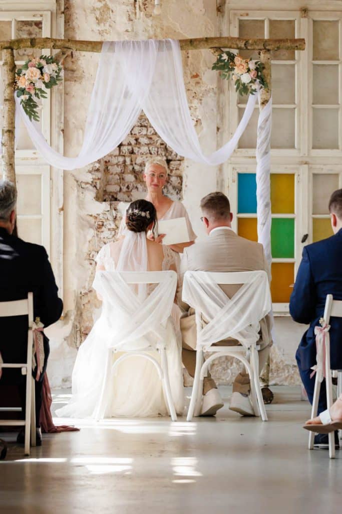 Freie Trauung in der stilvollen Orangerie von Schloss Diersfordt in Wesel: Das Brautpaar gibt sich vor Familie und Freunden das Ja-Wort in eleganter, lichtdurchfluteter Umgebung. Blumendekoration, romantisches Ambiente und die besondere Location machen diesen Moment einzigartig. Festgehalten vom Hochzeitsfotograf Wesel.