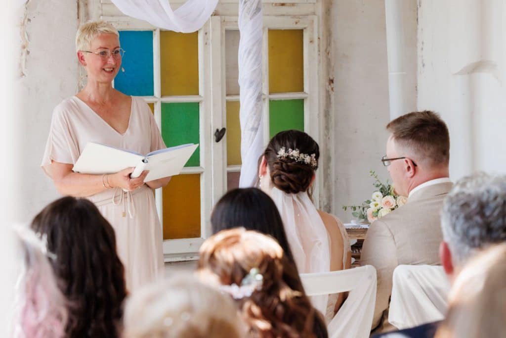 Freie Trauung in der stilvollen Orangerie von Schloss Diersfordt in Wesel: Das Brautpaar gibt sich vor Familie und Freunden das Ja-Wort in eleganter, lichtdurchfluteter Umgebung. Blumendekoration, romantisches Ambiente und die besondere Location machen diesen Moment einzigartig. Festgehalten vom Hochzeitsfotograf Wesel.