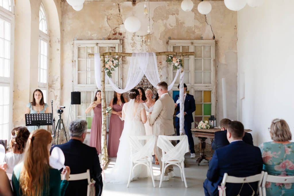 Freie Trauung in der stilvollen Orangerie von Schloss Diersfordt in Wesel: Das Brautpaar gibt sich vor Familie und Freunden das Ja-Wort in eleganter, lichtdurchfluteter Umgebung. Blumendekoration, romantisches Ambiente und die besondere Location machen diesen Moment einzigartig. Festgehalten vom Hochzeitsfotograf Wesel.