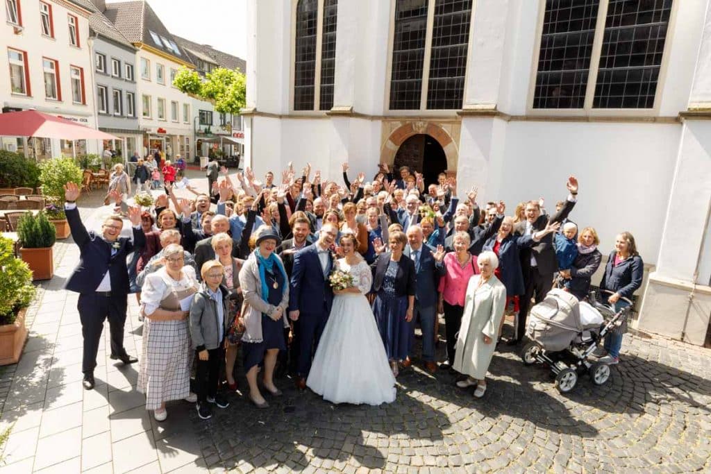 Fröhliche Gruppenfotos nach der Hochzeit in Xanten: Das Brautpaar posiert mit Familie und Freunden vor der Kirche. Lächelnde Gesichter, elegante Outfits und die festliche Stimmung machen die Gruppenfotos zu einer bleibenden Erinnerung. Fotografiert vom Hochzeitsfotograf Xanten.