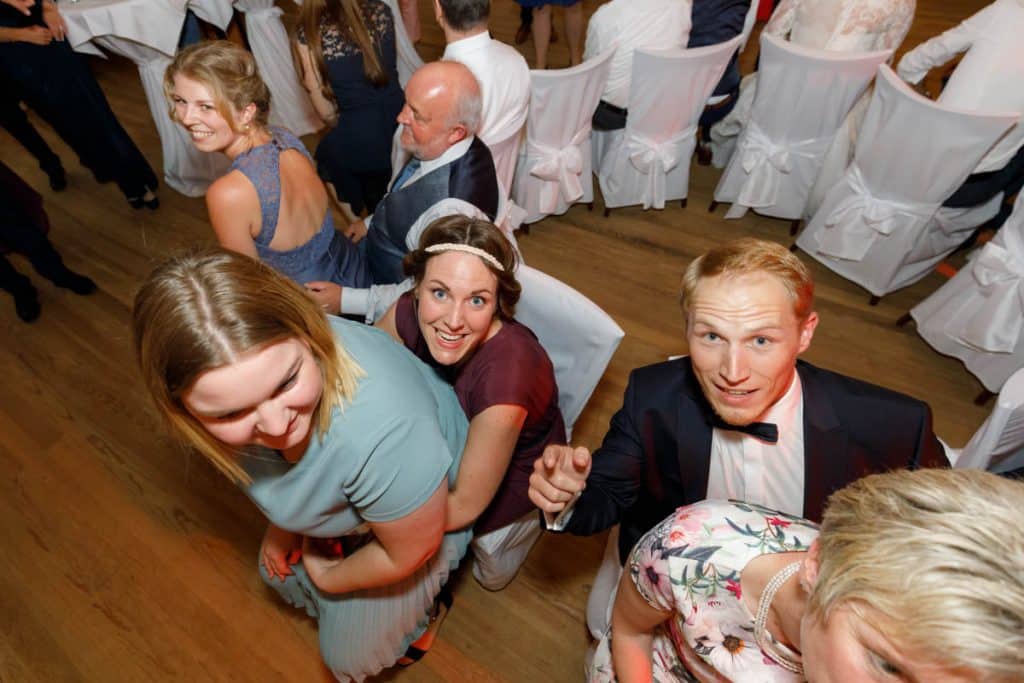Stimmungsvolle Hochzeitsfeier im Alten Schützenhaus in Xanten: Das Brautpaar tanzt ausgelassen mit Familie und Freunden. Die festlich geschmückte Location, lachende Gäste und Musik schaffen eine lebendige Atmosphäre voller Emotionen. Dieses Foto zeigt die authentische Hochzeitsreportage vom Hochzeitsfotograf Xanten.