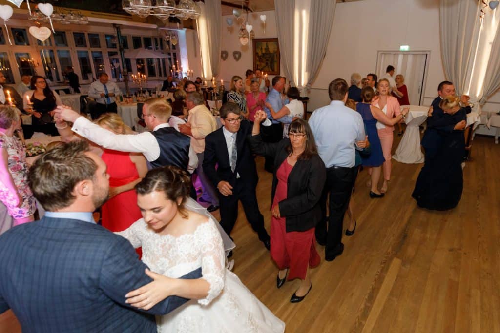 Stimmungsvolle Hochzeitsfeier im Alten Schützenhaus in Xanten: Das Brautpaar tanzt ausgelassen mit Familie und Freunden. Die festlich geschmückte Location, lachende Gäste und Musik schaffen eine lebendige Atmosphäre voller Emotionen. Dieses Foto zeigt die authentische Hochzeitsreportage vom Hochzeitsfotograf Xanten.