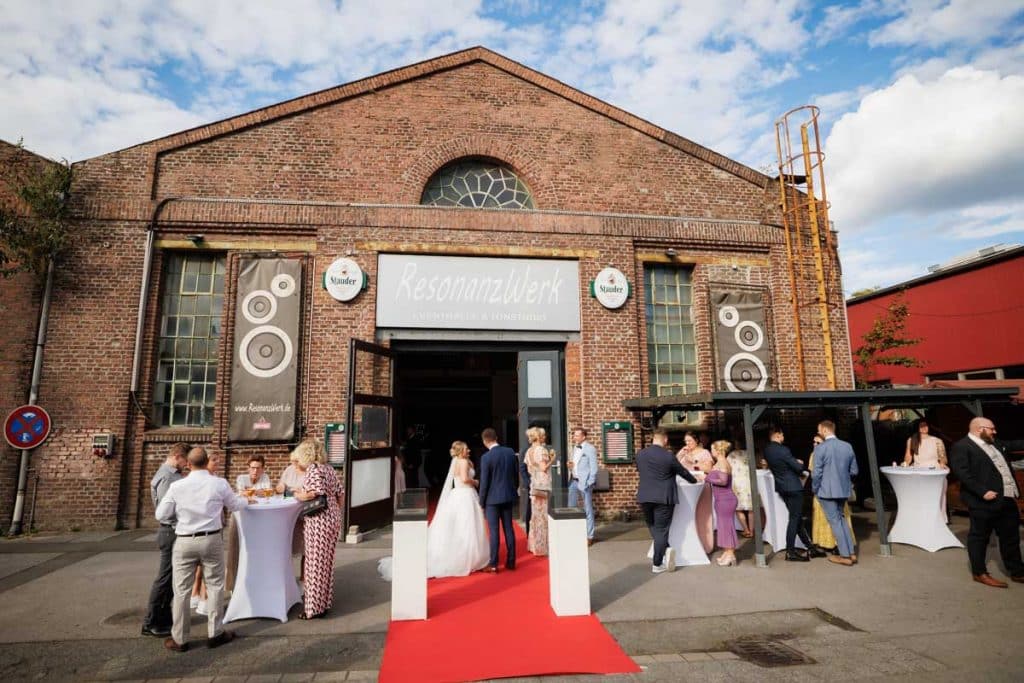 Ausgelassene Hochzeitsfeier im Resonanzwerk Oberhausen: Das Brautpaar eröffnet den Tanz, Gäste feiern ausgelassen auf der Tanzfläche und genießen das festliche Ambiente. Lebendige Reportagebilder voller Emotionen, aufgenommen vom Hochzeitsfotograf Duisburg.