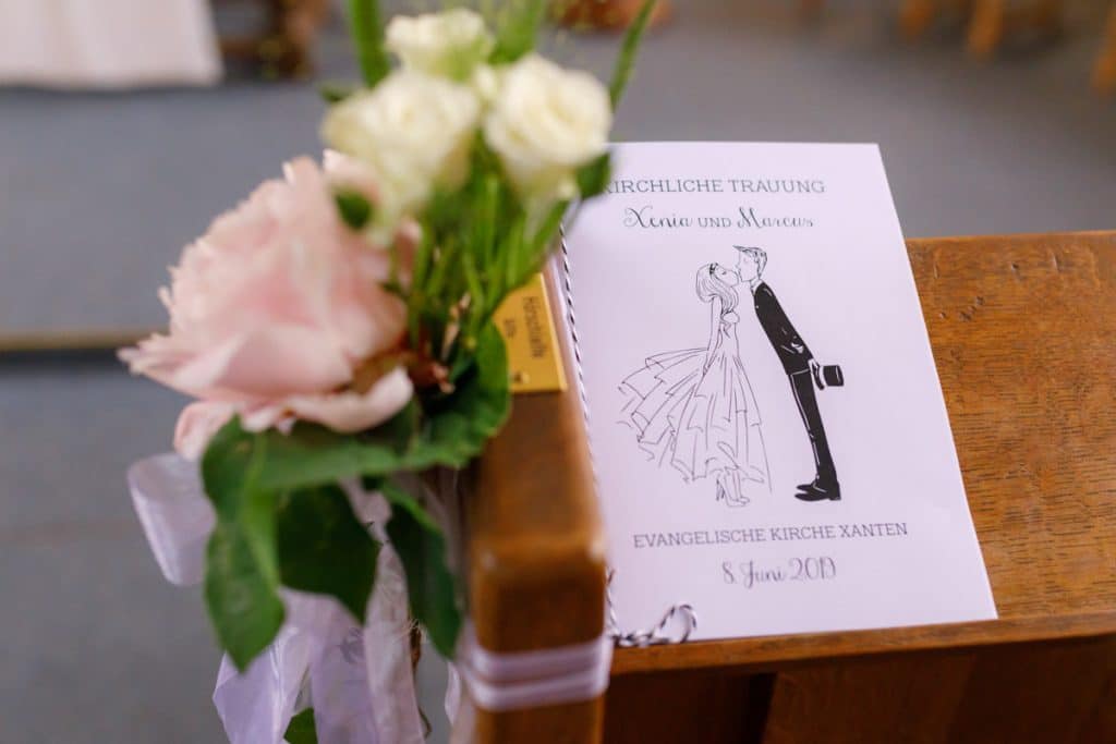 Emotionaler Moment bei der kirchlichen Trauung in der Evangelischen Kirche am Markt in Xanten: Das Brautpaar steht gemeinsam am Altar, die Braut im weißen Spitzenkleid mit Schleier, der Bräutigam im eleganten Anzug. Gäste verfolgen die Zeremonie aufmerksam in der festlich geschmückten Kirche. Dieses Foto zeigt die authentische Hochzeitsreportage vom Hochzeitsfotograf Xanten.