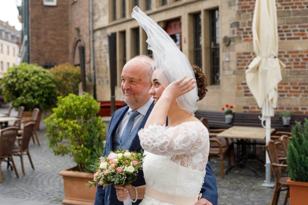 Emotionaler Moment bei der kirchlichen Trauung in der Evangelischen Kirche am Markt in Xanten: Das Brautpaar steht gemeinsam am Altar, die Braut im weißen Spitzenkleid mit Schleier, der Bräutigam im eleganten Anzug. Gäste verfolgen die Zeremonie aufmerksam in der festlich geschmückten Kirche. Dieses Foto zeigt die authentische Hochzeitsreportage vom Hochzeitsfotograf Xanten.