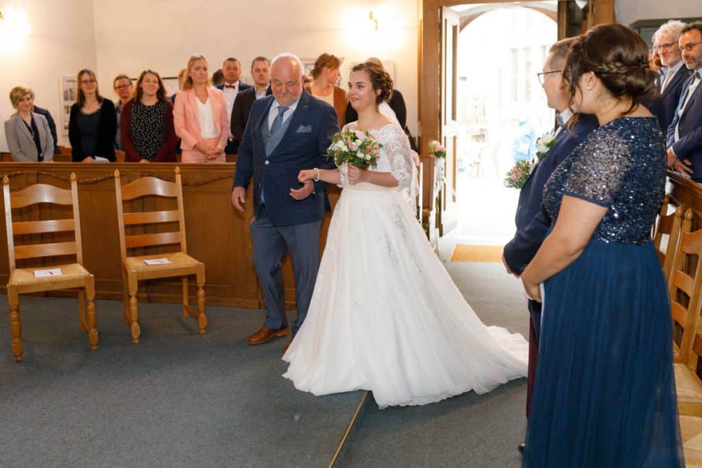 Emotionaler Moment bei der kirchlichen Trauung in der Evangelischen Kirche am Markt in Xanten: Das Brautpaar steht gemeinsam am Altar, die Braut im weißen Spitzenkleid mit Schleier, der Bräutigam im eleganten Anzug. Gäste verfolgen die Zeremonie aufmerksam in der festlich geschmückten Kirche. Dieses Foto zeigt die authentische Hochzeitsreportage vom Hochzeitsfotograf Xanten.