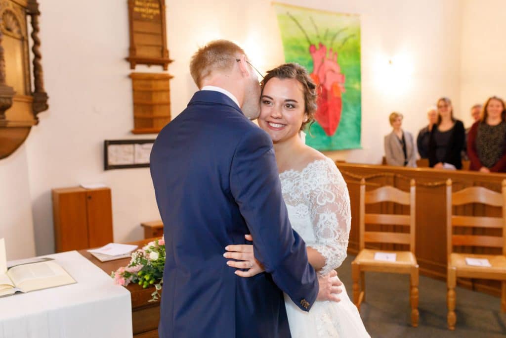 Emotionaler Moment bei der kirchlichen Trauung in der Evangelischen Kirche am Markt in Xanten: Das Brautpaar steht gemeinsam am Altar, die Braut im weißen Spitzenkleid mit Schleier, der Bräutigam im eleganten Anzug. Gäste verfolgen die Zeremonie aufmerksam in der festlich geschmückten Kirche. Dieses Foto zeigt die authentische Hochzeitsreportage vom Hochzeitsfotograf Xanten.
