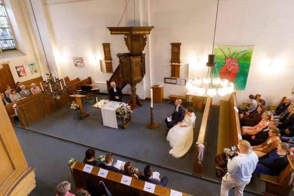 Emotionaler Moment bei der kirchlichen Trauung in der Evangelischen Kirche am Markt in Xanten: Das Brautpaar steht gemeinsam am Altar, die Braut im weißen Spitzenkleid mit Schleier, der Bräutigam im eleganten Anzug. Gäste verfolgen die Zeremonie aufmerksam in der festlich geschmückten Kirche. Dieses Foto zeigt die authentische Hochzeitsreportage vom Hochzeitsfotograf Xanten.