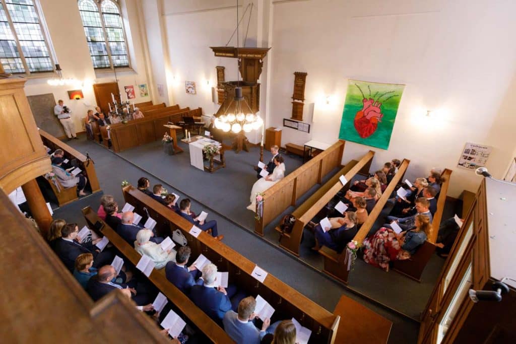 Emotionaler Moment bei der kirchlichen Trauung in der Evangelischen Kirche am Markt in Xanten: Das Brautpaar steht gemeinsam am Altar, die Braut im weißen Spitzenkleid mit Schleier, der Bräutigam im eleganten Anzug. Gäste verfolgen die Zeremonie aufmerksam in der festlich geschmückten Kirche. Dieses Foto zeigt die authentische Hochzeitsreportage vom Hochzeitsfotograf Xanten.