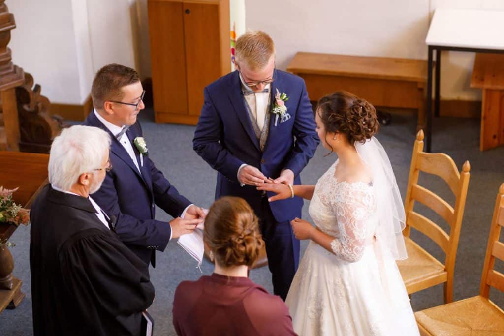 Emotionaler Moment bei der kirchlichen Trauung in der Evangelischen Kirche am Markt in Xanten: Das Brautpaar steht gemeinsam am Altar, die Braut im weißen Spitzenkleid mit Schleier, der Bräutigam im eleganten Anzug. Gäste verfolgen die Zeremonie aufmerksam in der festlich geschmückten Kirche. Dieses Foto zeigt die authentische Hochzeitsreportage vom Hochzeitsfotograf Xanten.
