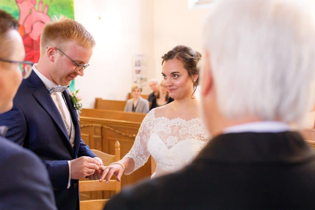 Emotionaler Moment bei der kirchlichen Trauung in der Evangelischen Kirche am Markt in Xanten: Das Brautpaar steht gemeinsam am Altar, die Braut im weißen Spitzenkleid mit Schleier, der Bräutigam im eleganten Anzug. Gäste verfolgen die Zeremonie aufmerksam in der festlich geschmückten Kirche. Dieses Foto zeigt die authentische Hochzeitsreportage vom Hochzeitsfotograf Xanten.