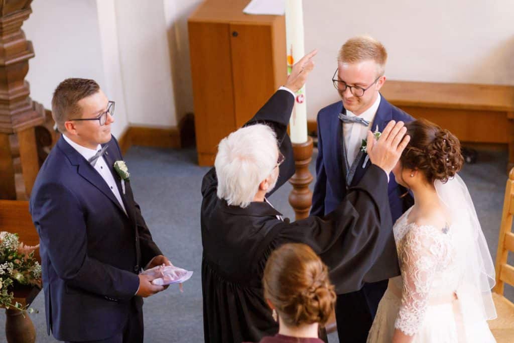 Emotionaler Moment bei der kirchlichen Trauung in der Evangelischen Kirche am Markt in Xanten: Das Brautpaar steht gemeinsam am Altar, die Braut im weißen Spitzenkleid mit Schleier, der Bräutigam im eleganten Anzug. Gäste verfolgen die Zeremonie aufmerksam in der festlich geschmückten Kirche. Dieses Foto zeigt die authentische Hochzeitsreportage vom Hochzeitsfotograf Xanten.