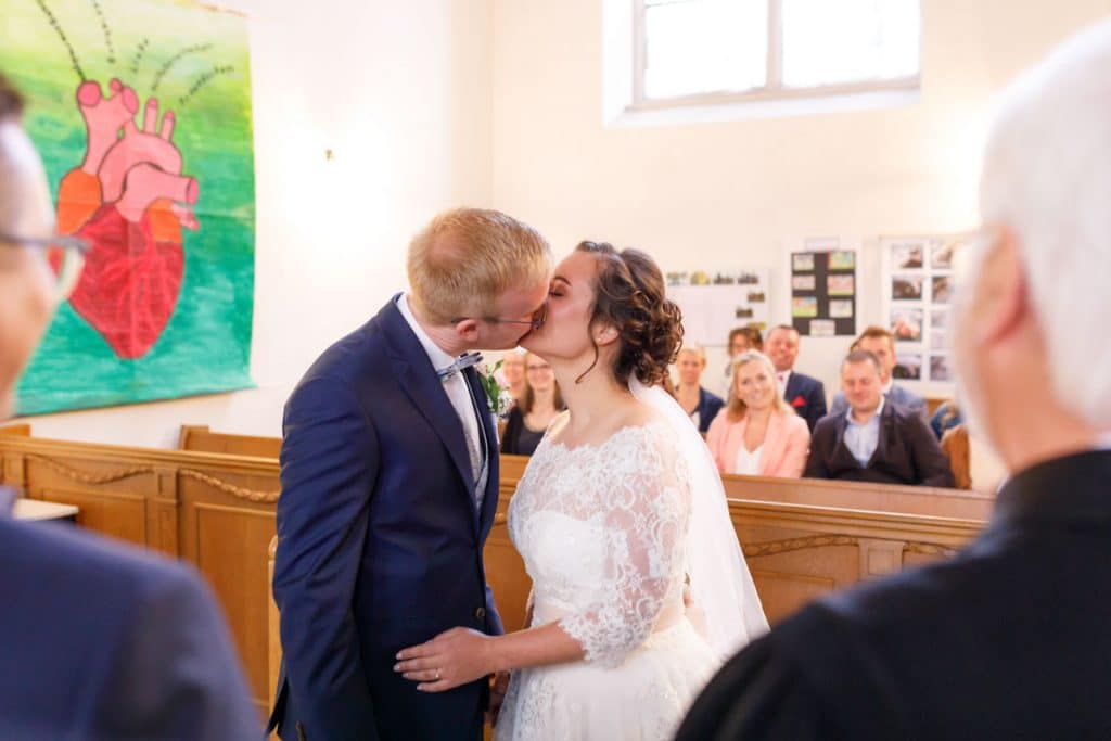 Emotionaler Moment bei der kirchlichen Trauung in der Evangelischen Kirche am Markt in Xanten: Das Brautpaar steht gemeinsam am Altar, die Braut im weißen Spitzenkleid mit Schleier, der Bräutigam im eleganten Anzug. Gäste verfolgen die Zeremonie aufmerksam in der festlich geschmückten Kirche. Dieses Foto zeigt die authentische Hochzeitsreportage vom Hochzeitsfotograf Xanten.