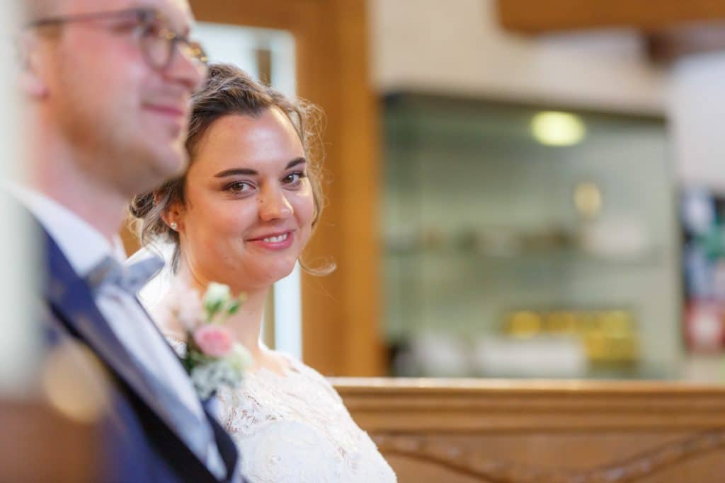 Emotionaler Moment bei der kirchlichen Trauung in der Evangelischen Kirche am Markt in Xanten: Das Brautpaar steht gemeinsam am Altar, die Braut im weißen Spitzenkleid mit Schleier, der Bräutigam im eleganten Anzug. Gäste verfolgen die Zeremonie aufmerksam in der festlich geschmückten Kirche. Dieses Foto zeigt die authentische Hochzeitsreportage vom Hochzeitsfotograf Xanten.